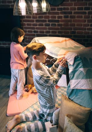 Boy helping lsister putting garland of lights in a tent