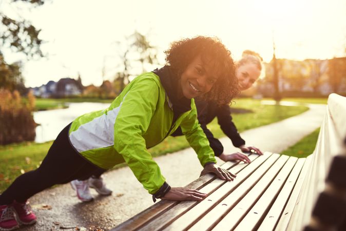 Two women smiling while doing an exercise on a park bench