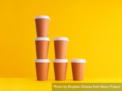 Declining stack of disposable coffee cups on yellow background 0JlYr4