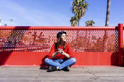 Woman in red sitting cross legged using a mobile phone outdoors on a bright day