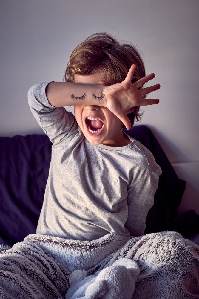 Unsatisfied boy refusing to sleep and covering eyes with hand
