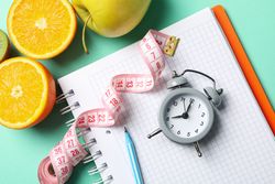 Notebook, measuring tape, alarm clock, pen and vegetarian food on mint background. Weight loss