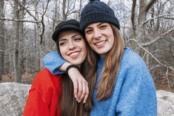 Smiling women in sweaters hugging in park
