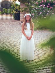 Smiling girl in white dress in park standing on pavement near tr