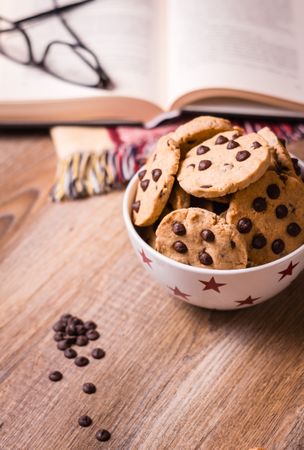 Chocolate chip cookies and book on wood background