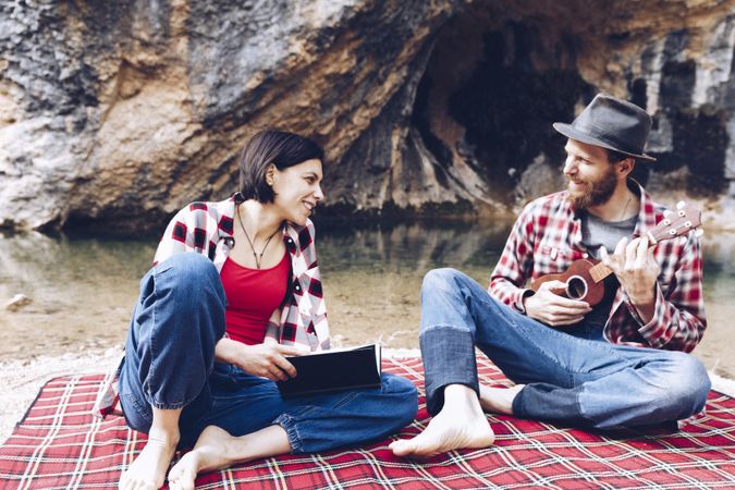 Chilling couple with book and guitar on shore