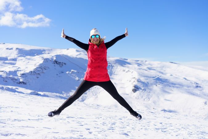 Woman in winter gear doing a star jump on snowy mountain