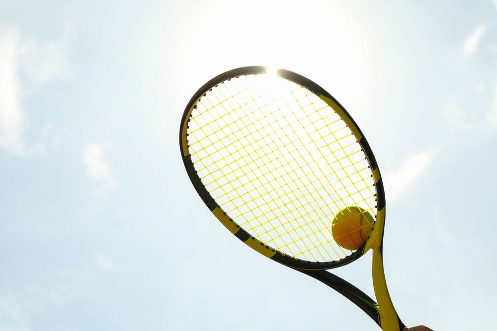 Tennis racquet with tennis ball against sky background