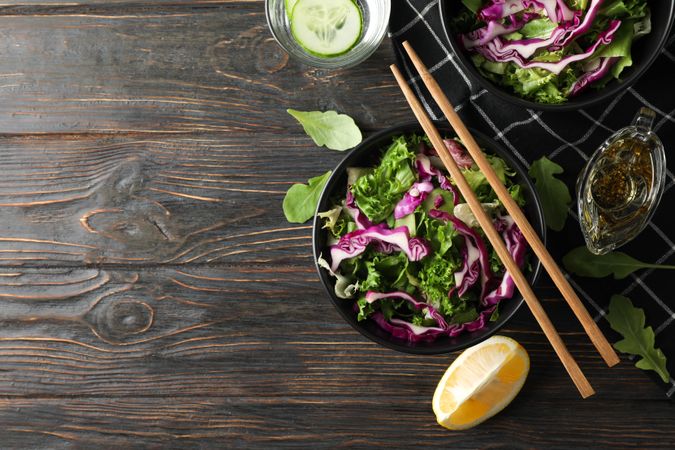 Black bowls with salad, chopsticks and towel on wooden background, top view