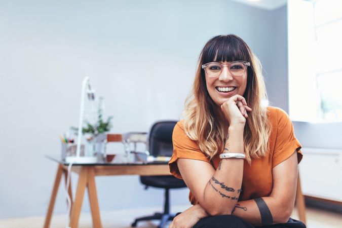 Smiling businesswoman sitting in office resting her chin on hand