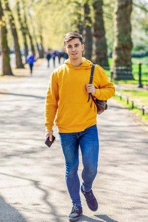 Man in yellow hoodie with backpack walking in park, vertical