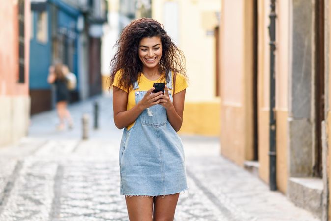 Smiling woman checking phone while strolling in front of metal door, copy space