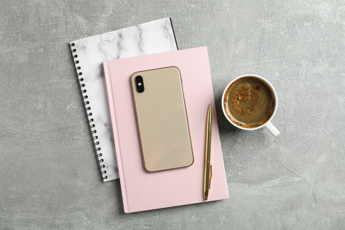 Cup of coffee with copybooks, phone and pen on grey background, top view