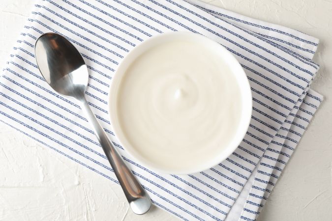 Bowl of sour cream yogurt, spoon and towel on cement background