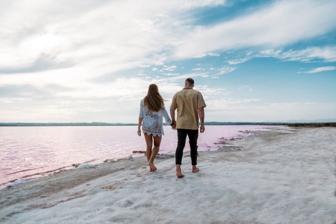 back view of adorable couple walking on an amazing beach with pink water