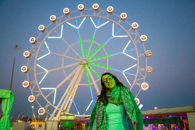 Smiling young woman near illuminated ferris wheel at night