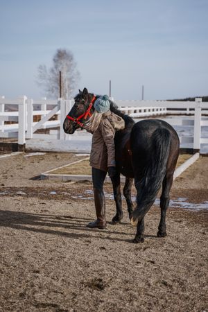 Warm dressed woman with brown horse by hay