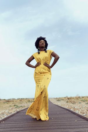 Woman in yellow sleeveless dress standing on asphalt road in desert