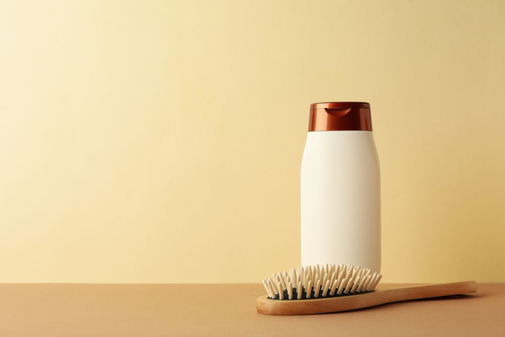 Blank shampoo bottle and hair brush on beige background