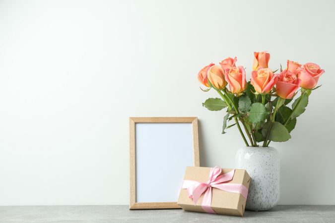 Vase with roses, gift and empty frame on grey table