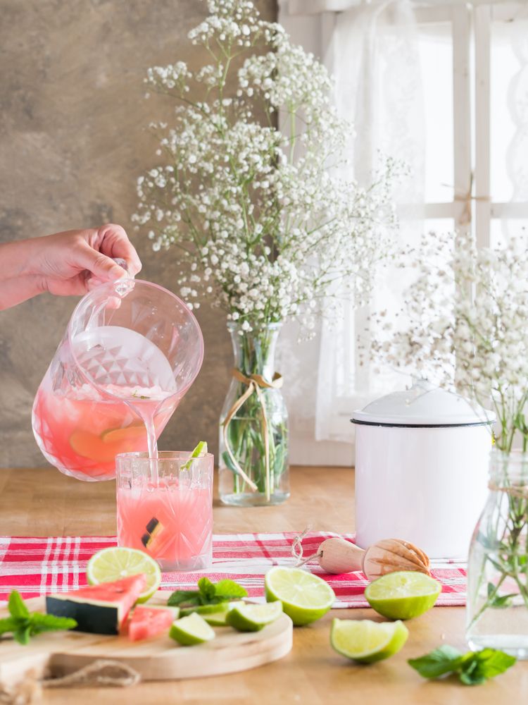Refreshing watermelon beverage with lime pouring into glass in kitchen