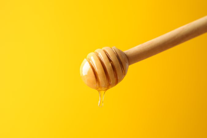 Dipper with honey on yellow background, space for text