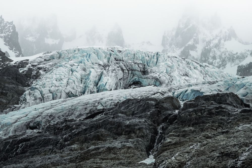 Gray rocky mountains with snow under foggy mist