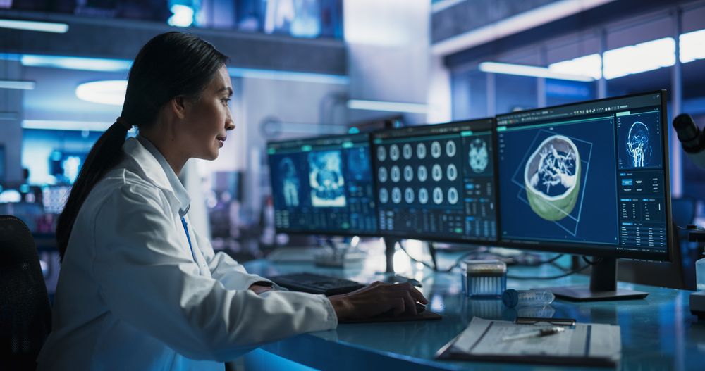 Female Asian Neuroscientist Using Desktop Computer With Human Brain CT Scans In Modern Medical Research Center Laboratory.