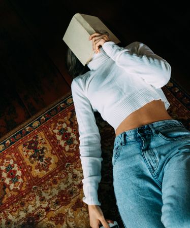 Woman in denim jeans holding a book unto her face laying on rug
