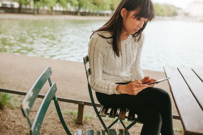 Shot of Asian woman at outdoor cafe by the pond using digital tablet