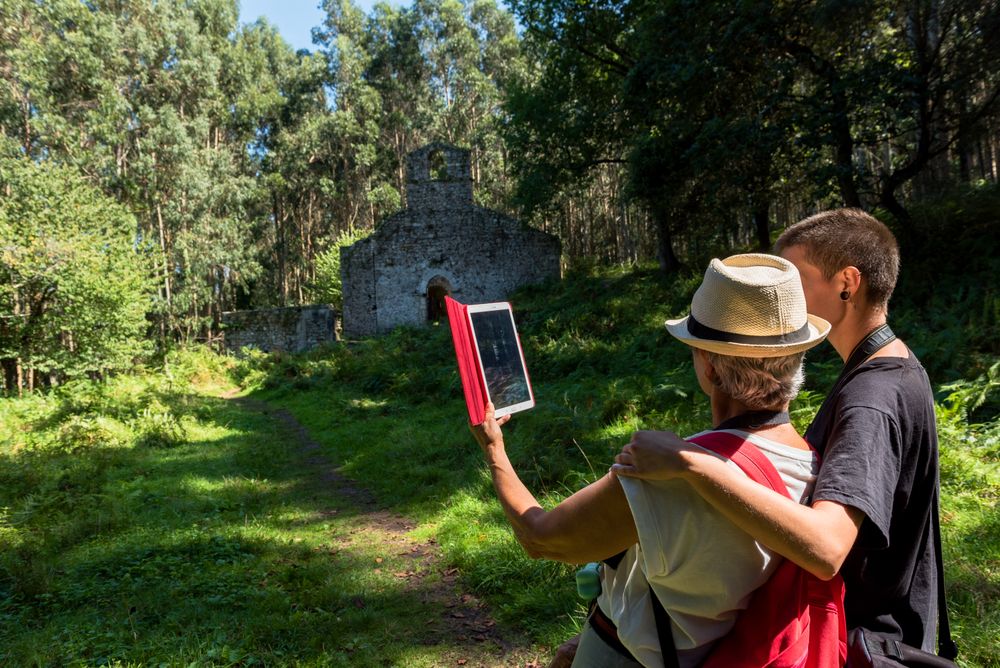 Young woman with arm around mature woman taking picture on tablet in forest