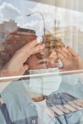 Serious child in mask observing city through window
