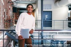 Happy young businessman smiling in a modern office leaning against railings in modern office 4M1BE4