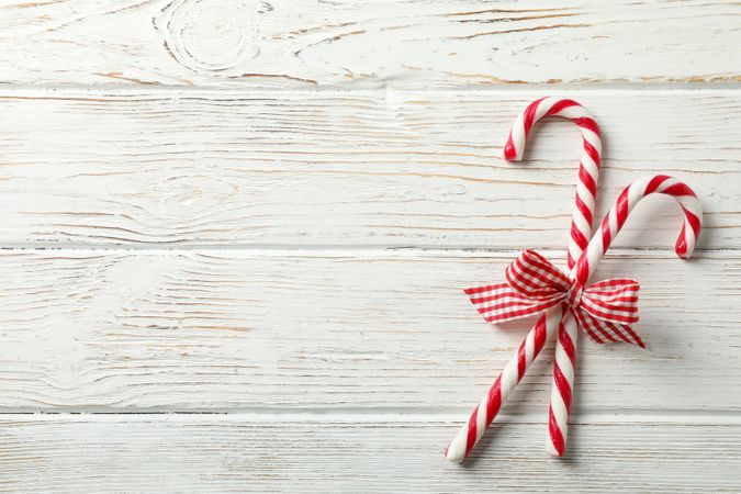 Sweet candy canes with bows on wooden background, space for text
