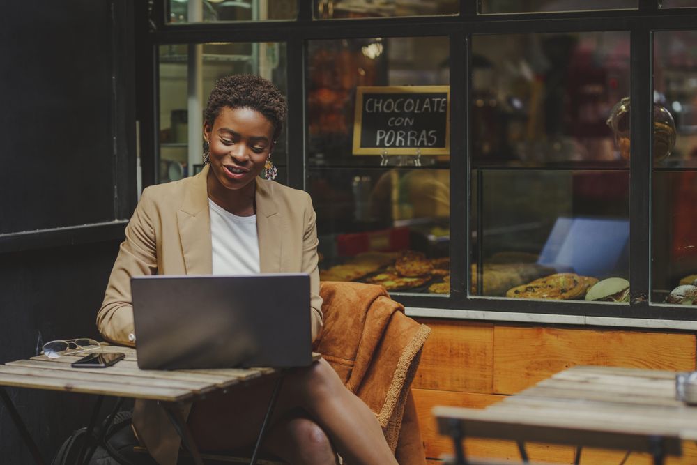 Smiling Black woman sitting at table with laptop in cafe