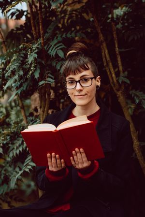 Young woman reading book on bench in park