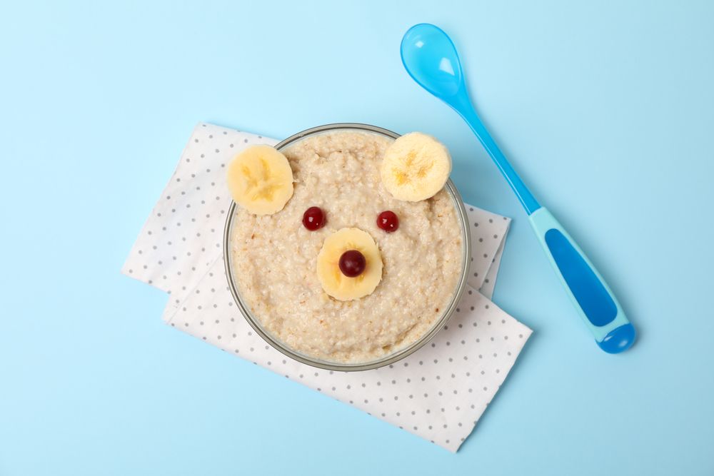 Bear face made of porridge and fruits on blue background, top view. Baby food