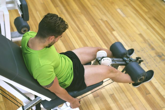 Top view of fit male in green t-shirt working out using leg extension machine, copy space