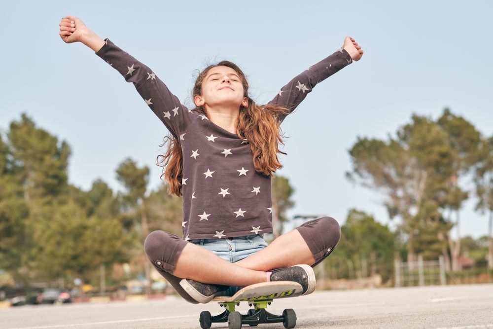 Excited girl sitting with outstretched arms on skateboard