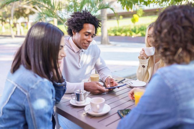 Black male looking at phone of with friends over coffee and juice outside