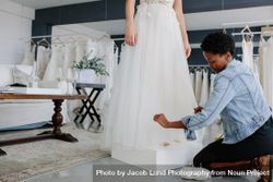 Female wedding dress designer making adjustment to bridal gown in her studio 56KWV4