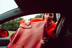 Woman putting suitcase in front window of car
