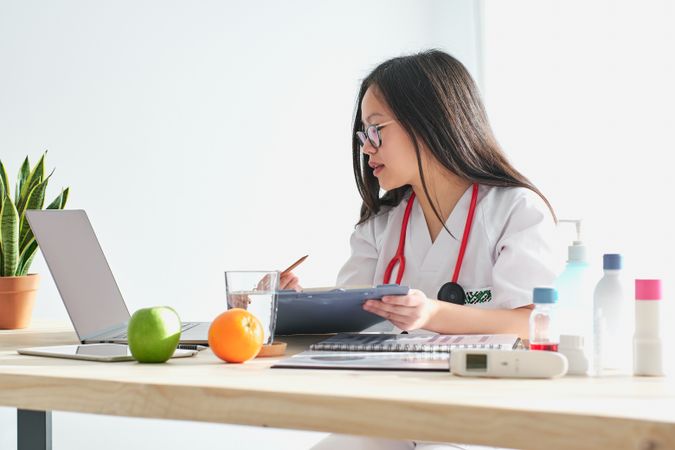 Asian doctor with documents browsing laptop in hospital