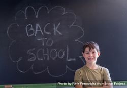Smiling boy standing at board with "back to school" written in chalk bDr8J5