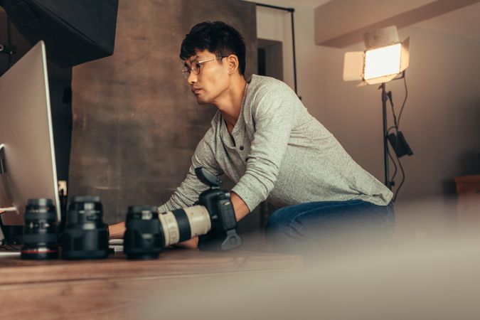 Photographer reviews photos on computer next to lenses