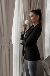 Side view of woman in blazer enjoying morning coffee by the window