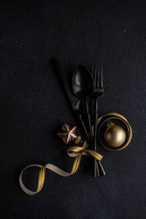 Dark cutlery on dark background tied with festive gold ribbon and ornaments