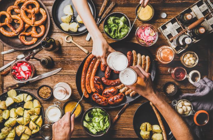 German sausages and pretzels displayed on wooden table with hands holding beer