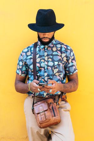 Stylish Black man using smartphone outdoors over yellow background