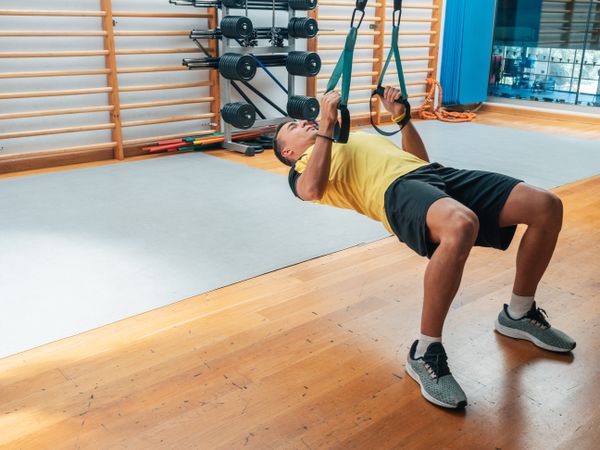 Strong man hanging with suspension ropes